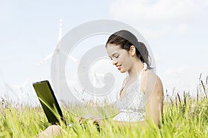 Teen girl with laptop next to wind turbine.