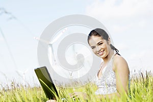 Teen girl with laptop next to wind turbine.