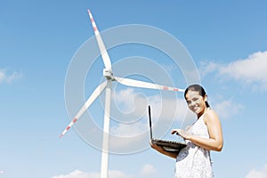 Teen girl with laptop next to wind turbine.