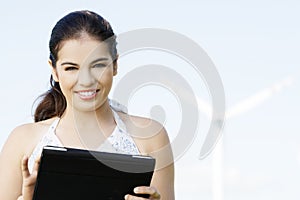 Teen girl with laptop next to wind turbine.