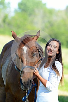 A teen girl laughs with her horse while out in a field.