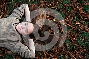 Teen girl laying on autumn ground with long hair scattered on grass.