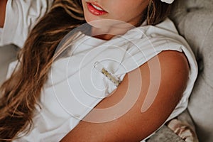 Teen girl laying on grey sofa using the thermometer and white compress. Copy space