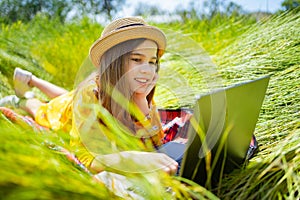 Teen girl learns working on laptop lying on meadow. mobile Internet in rural