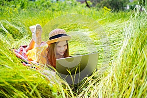 Teen girl learns working on laptop lying on meadow. mobile Internet in rural