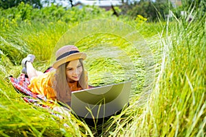 Teen girl learns working on laptop lying on meadow. mobile Internet in rural