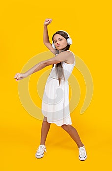 teen girl listen music in headphones and danc on yellow background