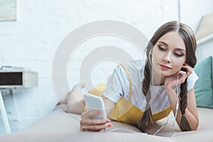 teen girl listening music with earphones and smartphone while lying photo