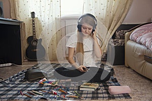 Teen girl listening to music in headphones using smartphone sitting on the floor at home