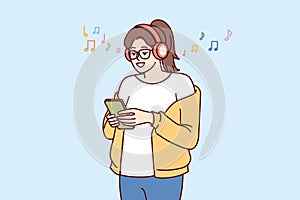 Teen girl listens music on headphones and holds phone with application to select track from playlist