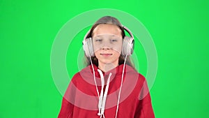 Teen girl listens to music and moving in large white headphones on green background. Slow motion