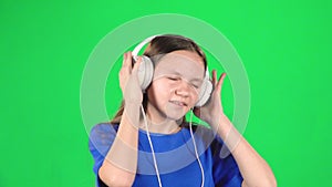 Teen girl listens to music and moving in large white headphones on green background. Slow motion