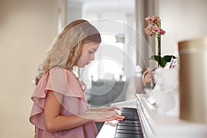 Teen girl long hair playing piano at home, dressed in pink