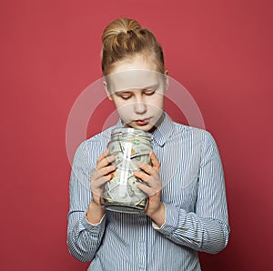 Teen girl looking at money cash in jar on pink background