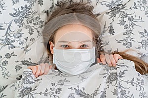 Teen girl lying in bed in a medical mask. top view