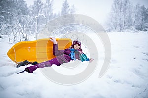 A teen girl is lying on the snow with the sled