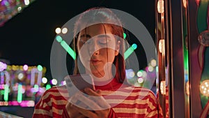 Teen girl making call in neon luna park closeup. Pretty girl resting amusement