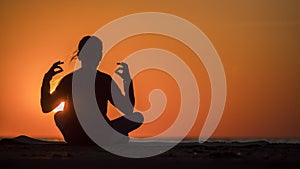 Teen girl meditating in lotus position at sunset. Sitting by the sea on a background of orange sky