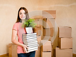 Teen girl moving house to college, holding pile books and plant