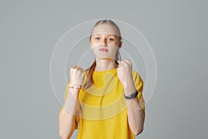 Teen girl with negative facial expression raising fists furiously looking at the camera, isolated on light grey background,