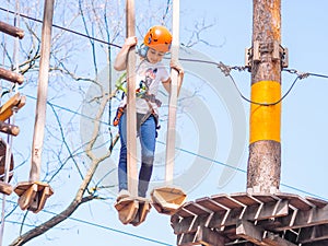 Teen girl in orange helmet climbing in trees in forest adventure park
