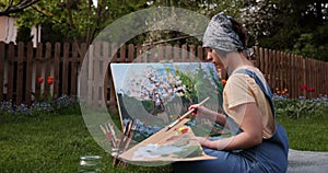 Teen girl painting on canvas in the garden .