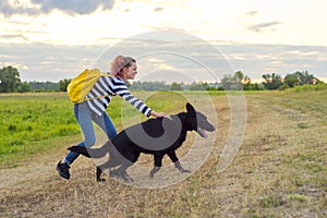 Teen girl pet owner playing and talking with big black shepherd dog