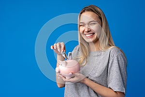 Teen girl with piggy bank on blue background.