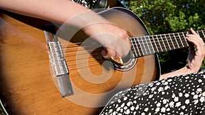 Teen girl playing acoustic guitar, close up. Woman practices guitar chords outdoors