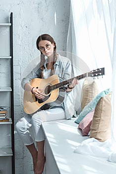 teen girl playing acoustic guitar while sitting photo