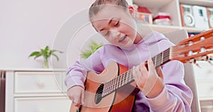 Teen girl is playing guitar and singing, sitting on the floor.