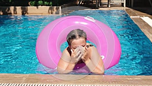 Teen girl playing with pink inflatable ring in swimming pool. Girl rubbing her eyes after diving. Slow motion