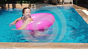 Teen girl playing with pink inflatable ring in swimming pool. Girl splashing water and diving under water. Slow motion