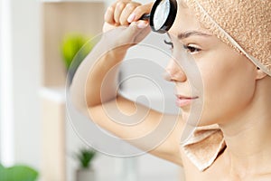 Teen girl with problem skin look at pimple with magnifying glass.