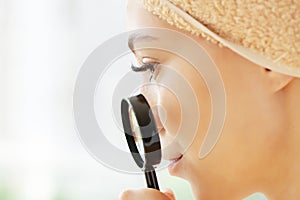 Teen girl with problem skin look at pimple with magnifying glass.