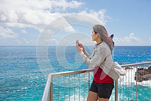 Teen girl at railing taking pictures by tropical ocean