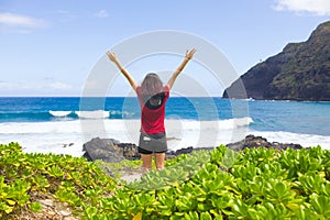 Teen girl raising arms in praise standing by ocean shore