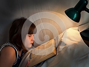 Teen girl reading book on bed at night