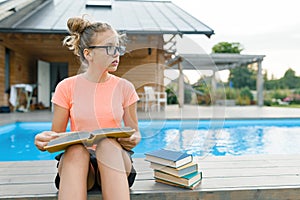 Teen girl reading book, girl alone in private area near the house and pool
