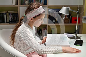 Teen girl reads book while sitting at desk in his photo