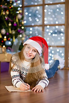 Teen girl in red christmas hat writes letter to Santa Claus