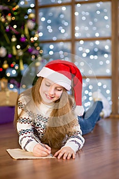 Teen girl in red christmas hat writes letter to Santa Claus