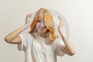 Teen girl with red hair in a white t-shirt on a light background laugh and straighten hair