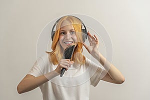 Teen girl with red hair in a white t-shirt on a light background listening to music with headphones and singing