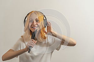 Teen girl with red hair in a white t-shirt on a light background listening to music with headphones and singing