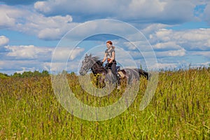 Beautiful redheaded girl riding a horse in countryside. .