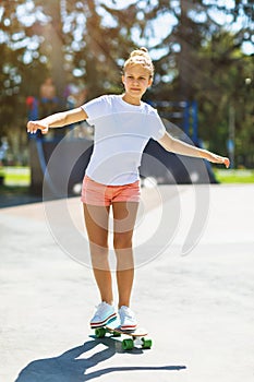 Teen girl rides a skateboard in the park on a summer sunny day