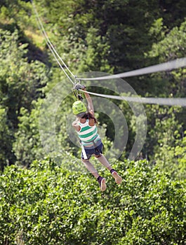 Teen girl riding a zipline through the forest. View from behind