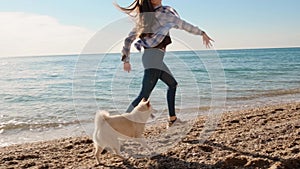 Teen girl run and play ball with her shiba inu beautiful pet on the sunny beach slow motion