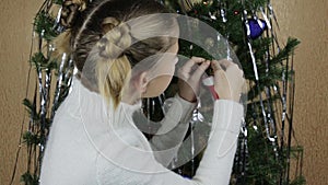 Teen girl secretly hangs on a Christmas tree miniature red mitten Santa Claus